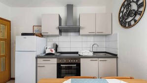 A compact kitchen with a refrigerator, stove, oven, and sink. There is a clock on the wall and a table with chairs. - Holiday apartment Cheap accommodation in a great location (Bašanija)