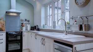 A modern kitchen with white cabinetry, a built-in oven, a large sink, and a window with a view of the outside. - Bulmer Cottage | Dog-Friendly Coastal Cottage, 10 Mins Walk to Beach (Winterton-on-Sea)