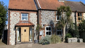 A two-story house with a stone facade, a wooden front door, and a tiled roof. - Bulmer Cottage | Dog-Friendly Coastal Cottage, 10 Mins Walk to Beach (Winterton-on-Sea)
