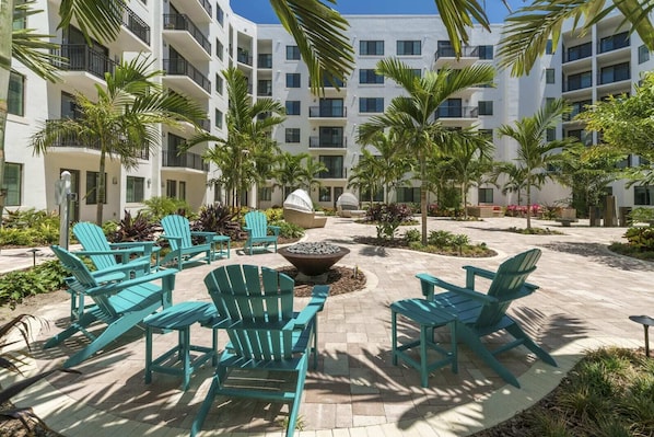 Relax in a serene courtyard surrounded by lush tropical plants and palm trees, with a cozy fire pit and stylish seating area.