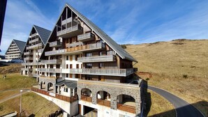 A multi-story hotel with balconies, stone arches, and a hilly backdrop. - 5159A (Besse-et-Saint-Anastaise)