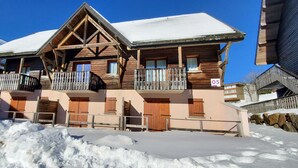 A wooden chalet with a balcony, a stone wall, and a snow-covered roof.