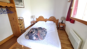 A bedroom with a wooden bed, two bedside tables with lamps, a radiator, and a window with curtains.