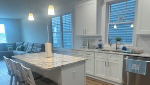 A modern kitchen with white cabinetry, a marble island, and bar stools.
