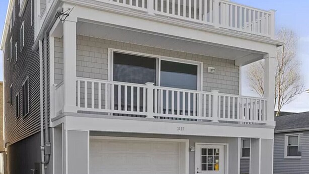 A two-story residential building with a white exterior, a balcony on the upper floor, and a garage at the front.