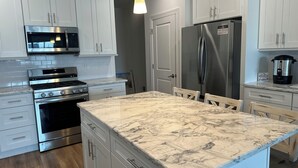 A modern kitchen with white cabinetry, stainless steel appliances, and a marble island.
