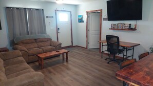 A living room with a sofa, a coffee table, a TV mounted on the wall, and a bookshelf with books. - Falling Water Cabin (witts springs)