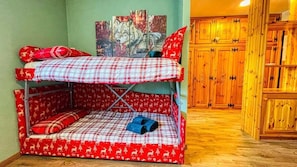 Una cama litera con colcha a cuadros rojo y blanco, una obra de arte con temática de lobo en la pared y armarios de madera al fondo.