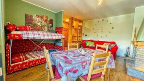 A cozy room with a bunk bed, a dining table, a red sofa, and a wooden cabinet.