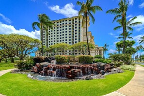 A hotel with a large building, a landscaped garden with a waterfall, and palm trees.