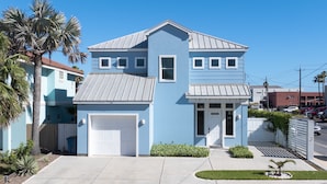 Ein zweistöckiges Haus mit Garage, einem kleinen Vorgarten mit Palmen und einem strahlend blauen Himmel.