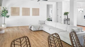 Ein modernes Wohnzimmer mit einem weißen Ecksofa, Korbstühlen und einem Essbereich mit Tisch.