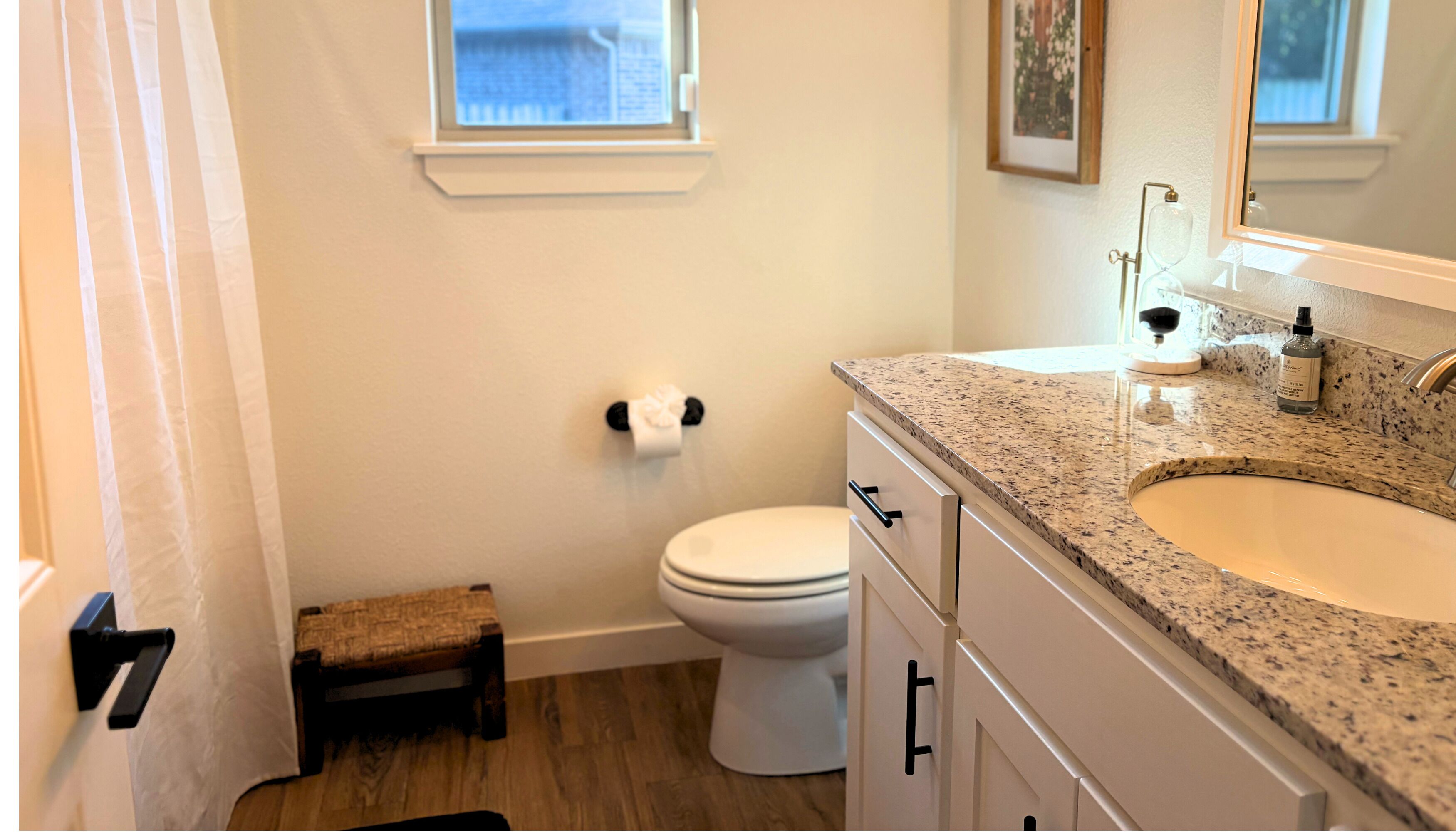 A bathroom with a white toilet, a small step stool, a granite countertop, a sink, and a mirror.