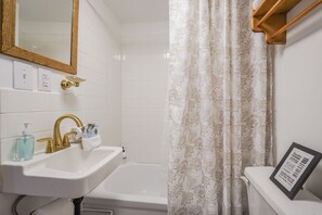 Une salle de bain avec un lavabo blanc, un robinet doré et un rideau de douche à motifs floraux.