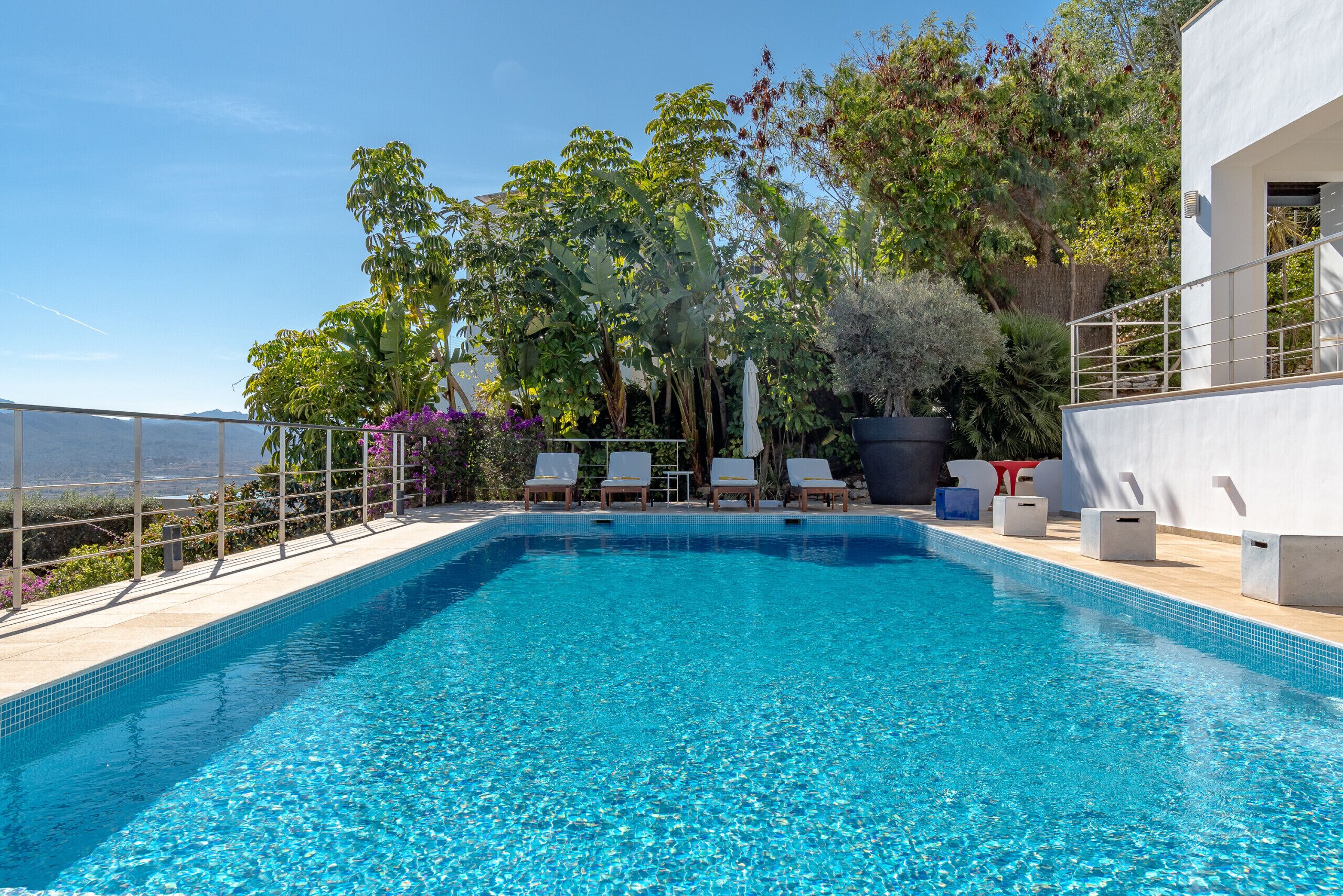 Une piscine d’un bleu éclatant, agrémentée de chaises longues et de plantes en pot.