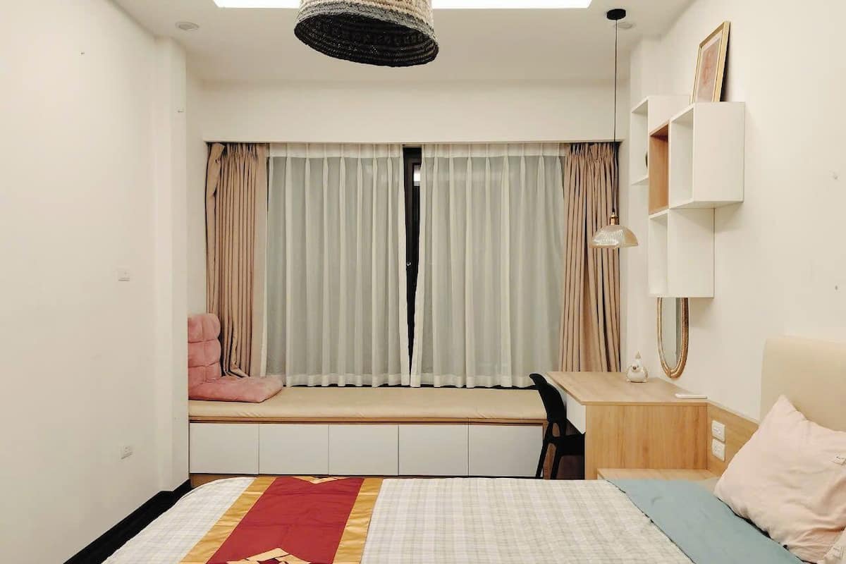 A bedroom with a bed, a desk, a chair, a window with curtains, and a built-in shelf.