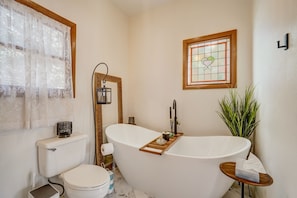 A bathroom with a freestanding bathtub, a toilet, a sink, a mirror, and a potted plant. - Garden Base B (Colorado Springs)