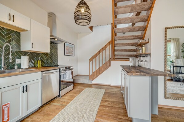 A modern kitchen with white cabinets, a wooden staircase, and a hanging light fixture.