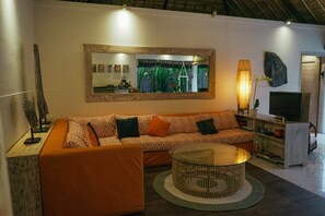 A modern living room with a sectional sofa, a round coffee table, a large mirror, and a television. - Villa Parianca (Canggu)