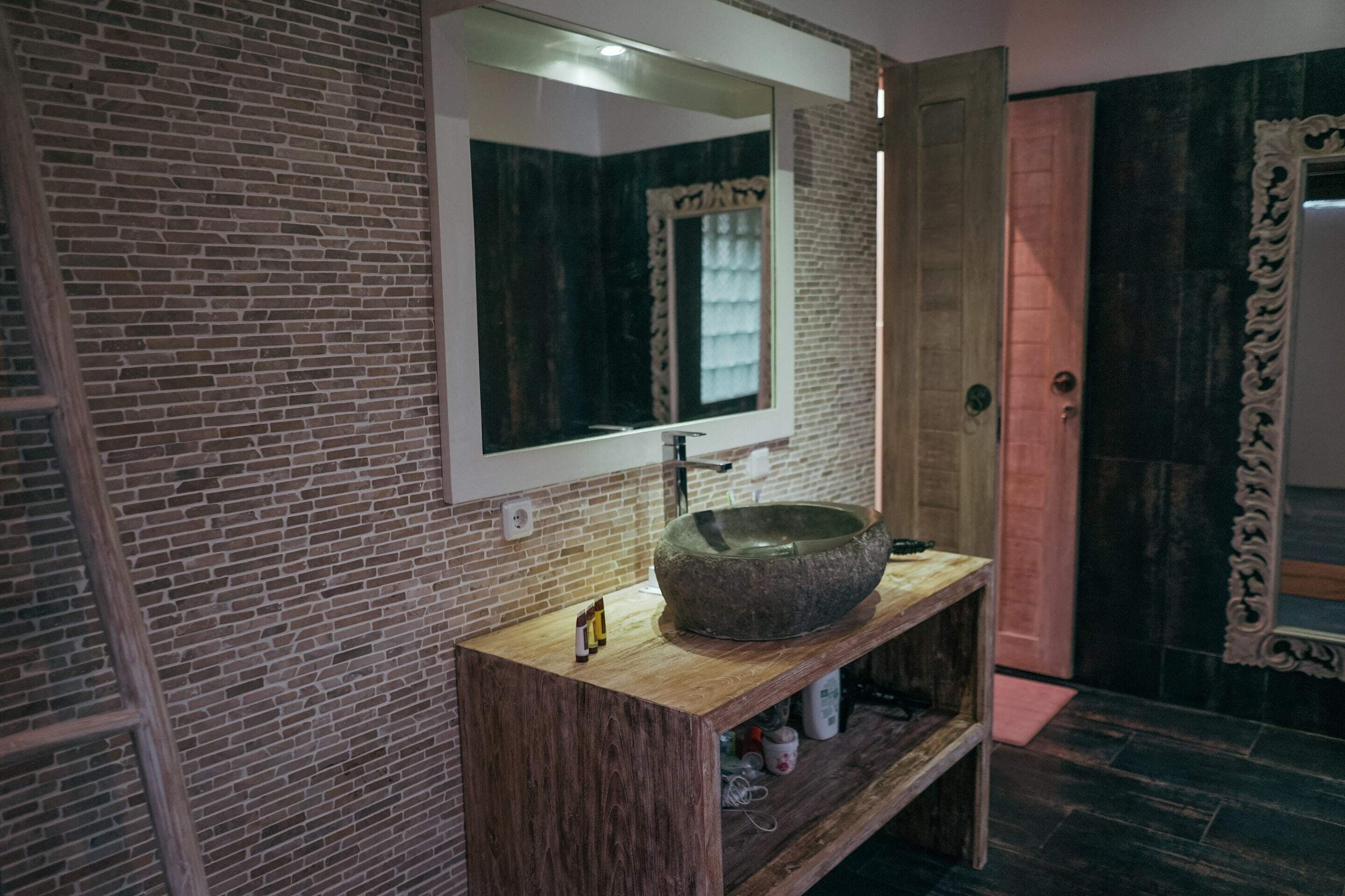 Un baño con lavamanos de piedra, tocador de madera y un espejo grande.