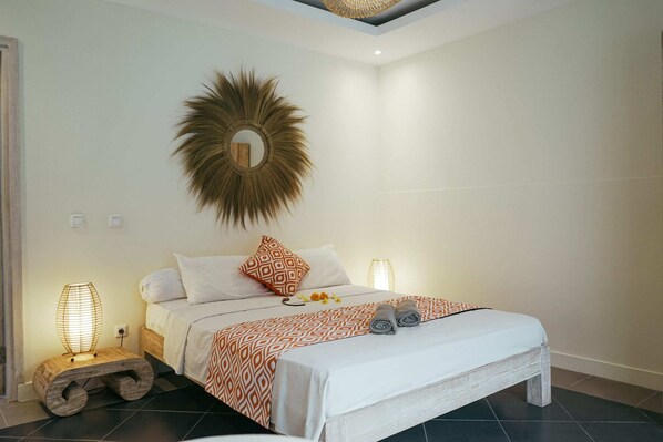 A neatly arranged bedroom with a bed, two bedside lamps, a decorative mirror, and a small wooden stool.