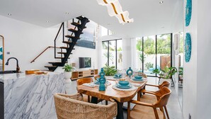 Een moderne keuken met een marmeren eiland, een eethoek met houten stoelen, en een trap naar een hoger niveau.