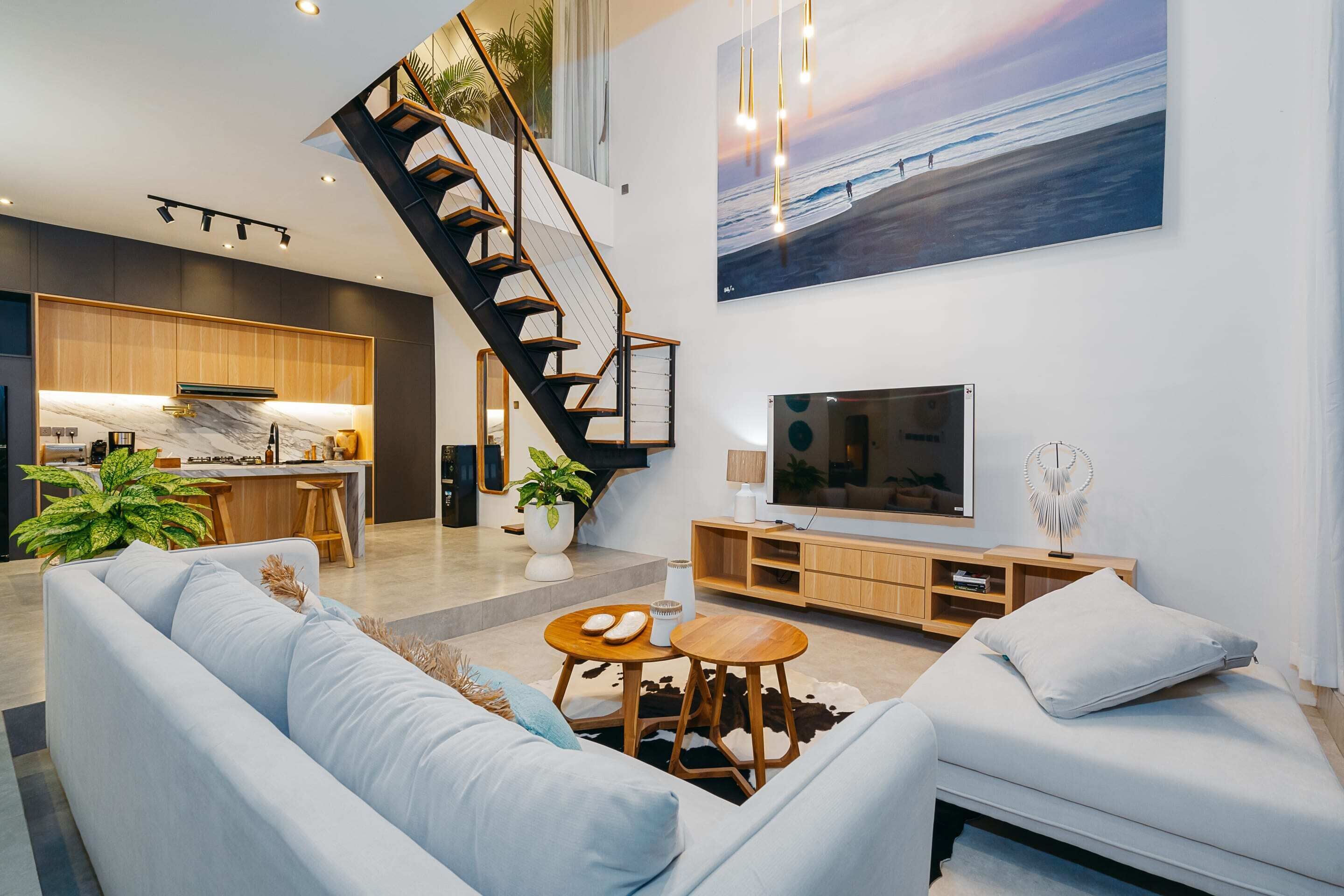 Ein modernes Wohnzimmer mit Treppe, großem Fernseher und einer Küche im Hintergrund.