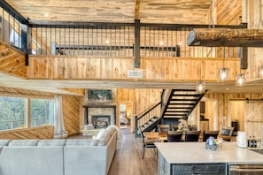 A spacious living area with a fireplace, a dining table with chairs, and a staircase leading to an upper level.