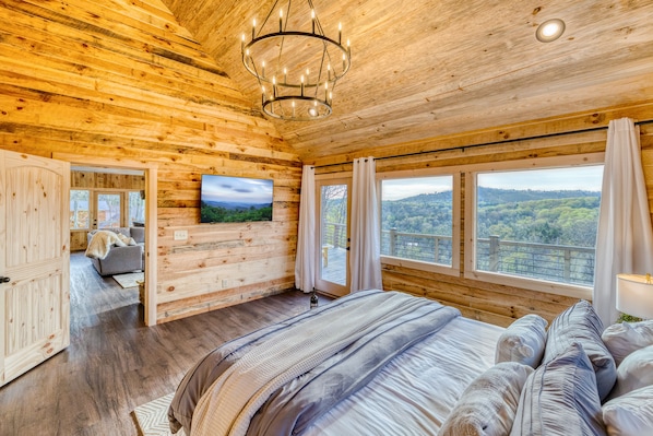 A wooden cabin bedroom with a large bed, a television, and a scenic view through the windows.