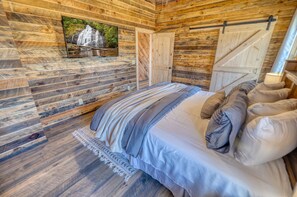A wooden cabin bedroom with a bed, pillows, a blanket, a picture of a waterfall, and a door.