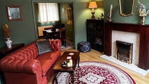 Ein Wohnzimmer mit einer roten Ledersofa, einem Holztisch, einem gemusterten Teppich, einem Kamin und einem Essbereich im Hintergrund.