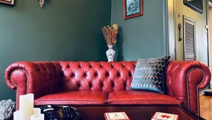 Ein rotes Ledersofa mit einem blau gemusterten Kissen, einer Vase mit Trockenblumen und einem Tablett für die Fernbedienung.