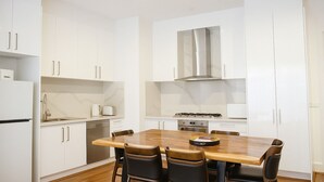 Una cocina compacta con armarios blancos, una mesa de comedor de madera y una estufa empotrada.