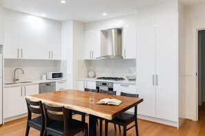 A modern kitchen with white cabinetry, a wooden dining table, and black chairs.