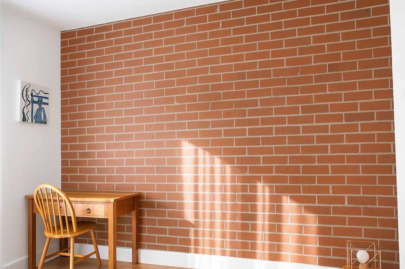 A room with a brick wall, a wooden desk, a chair, and a framed picture.
