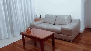 Una sala de estar con un sofá color beige, una mesa de centro de madera y una cortina blanca.