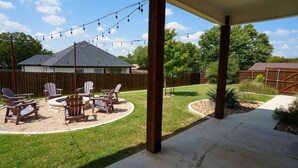 Un patio trasero con porche cubierto, zona de estar al aire libre con sillas Adirondack y un césped bien cuidado.