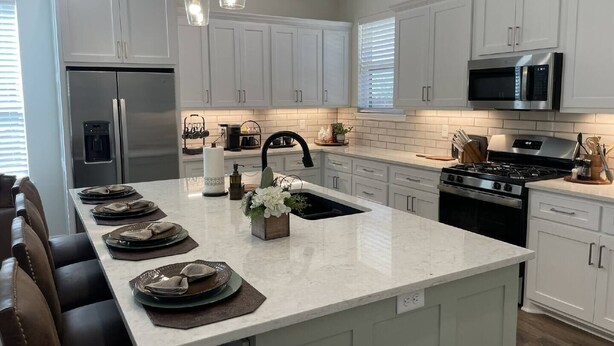 Una cocina moderna con armarios blancos, una isla central, electrodomésticos de acero inoxidable e iluminación colgante.
