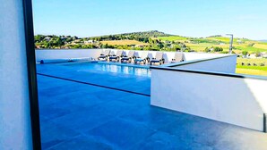 Une piscine sur le toit, dotée de chaises longues et offrant une vue sur un paysage verdoyant.