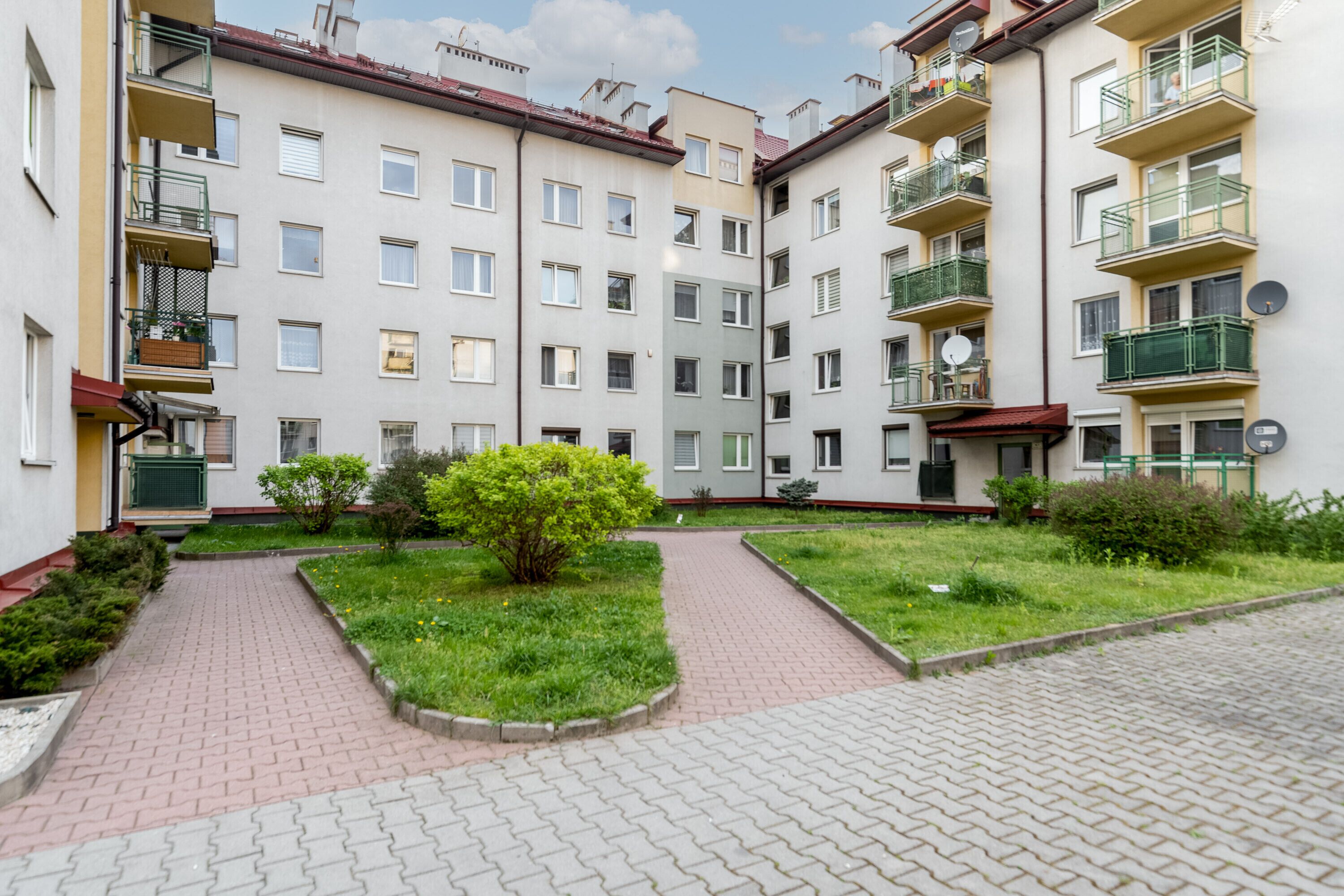 Um edifício residencial com vários andares, varandas, um jardim central e um caminho pavimentado.