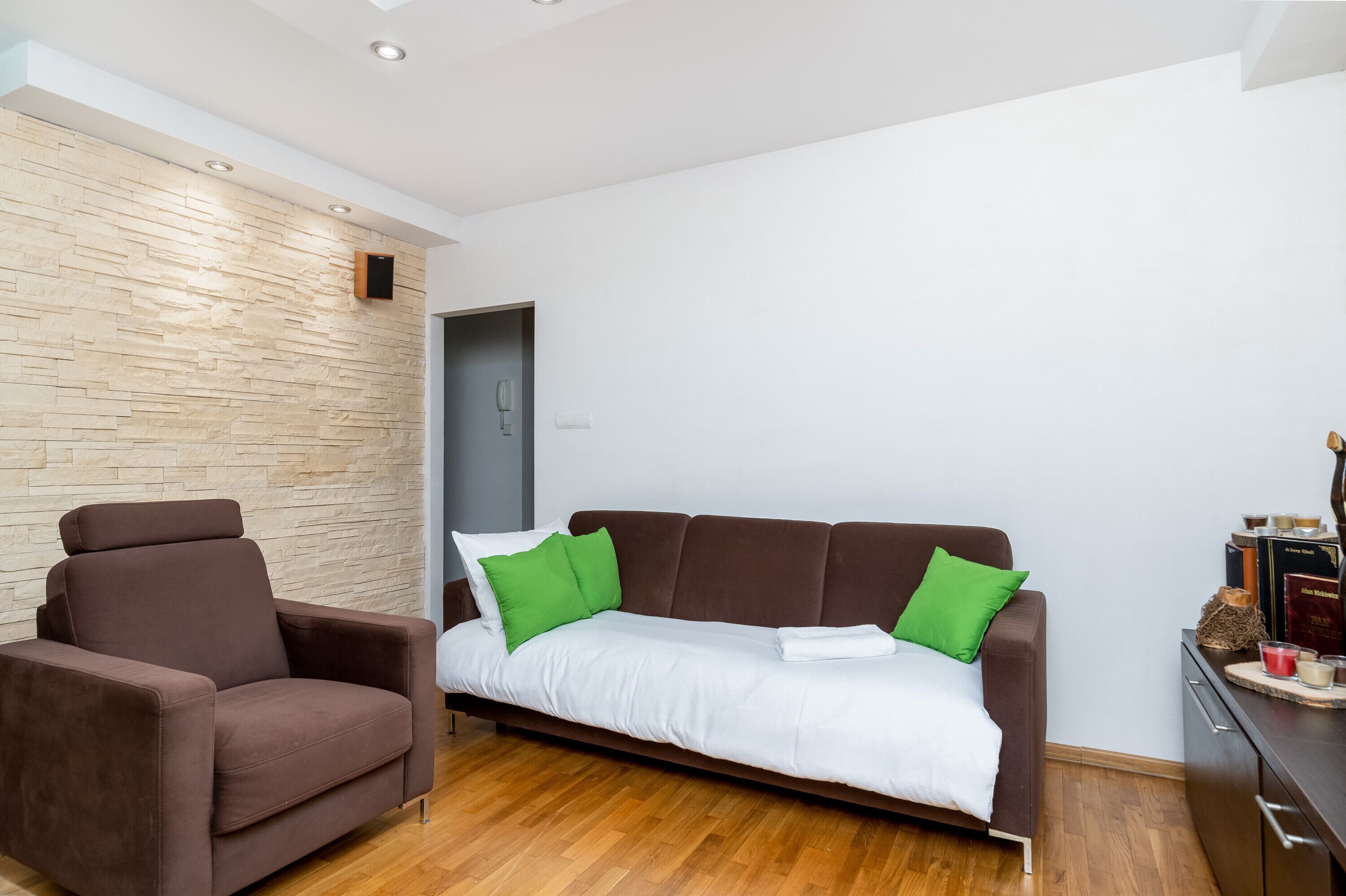 A modern living room with a brown sofa, a brown armchair, and a white wall with a wooden panel design.