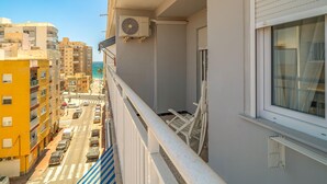 Ein Balkon mit Blick auf eine belebte Straße und Gebäude, einer Klimaanlage und einem Fenster mit Jalousien.