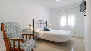 Ein Schlafzimmer mit Bett, Sessel, Nachttisch mit Lampen und einem an der Wand befestigten Fernseher.