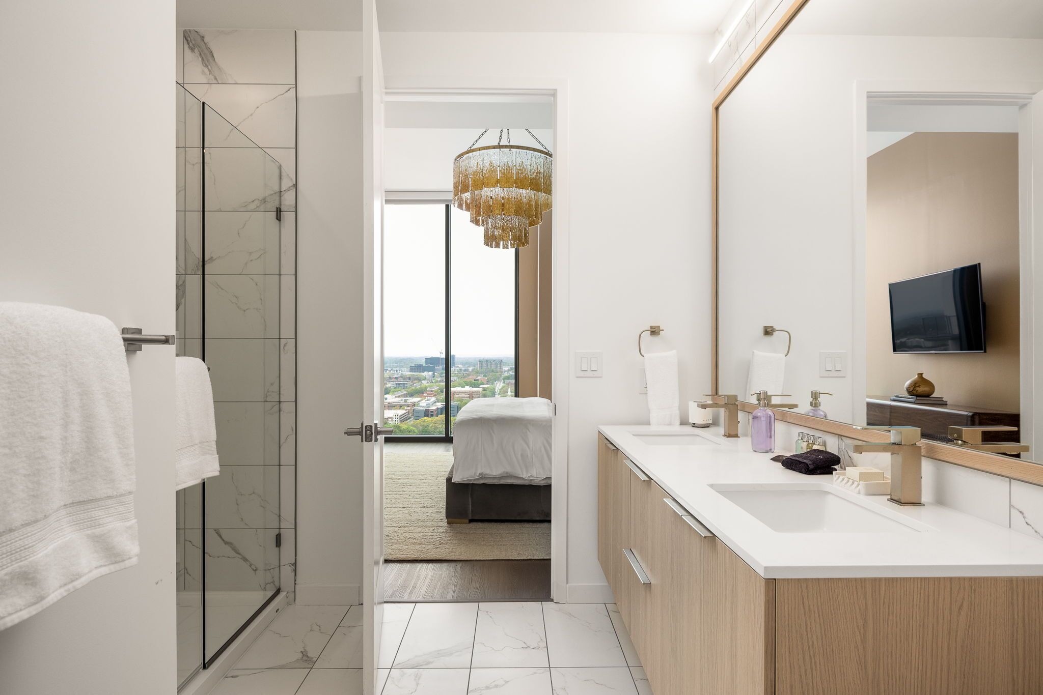 A modern bathroom with a glass shower, a large mirror, and a view to the outside.