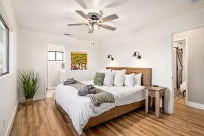 Une chambre à coucher avec un lit en bois, un ventilateur de plafond, une table de chevet et un tableau accroché au mur.