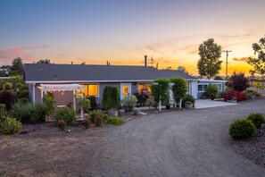 Une maison de plain-pied dotée d’un patio couvert, entourée de diverses plantes et arbustes.