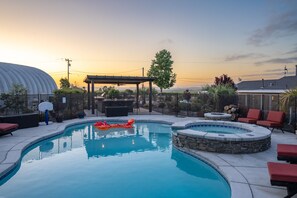 Une piscine avec un jacuzzi, des chaises longues rouges et une pergola.