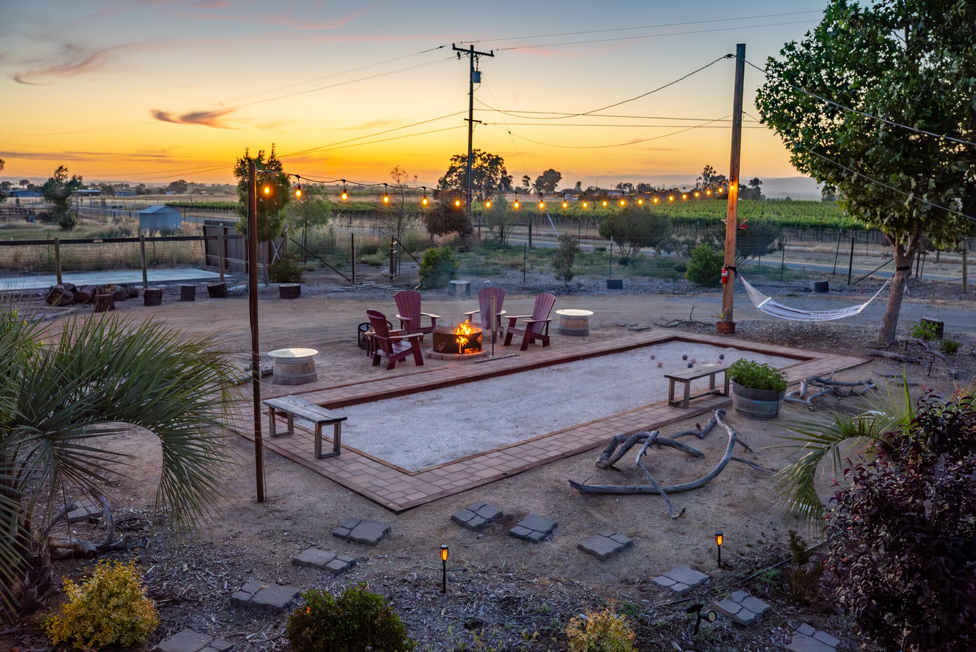 An outdoor patio area with a fire pit, seating, and string lights.