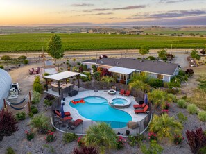 A pool area with lounge chairs and a hot tub, surrounded by a landscaped garden and a house. - Vineyard Oasis: Pool & Views! (Paso Robles)