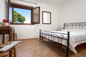 A bedroom with a bed, a desk with books, a window, and a mirror.